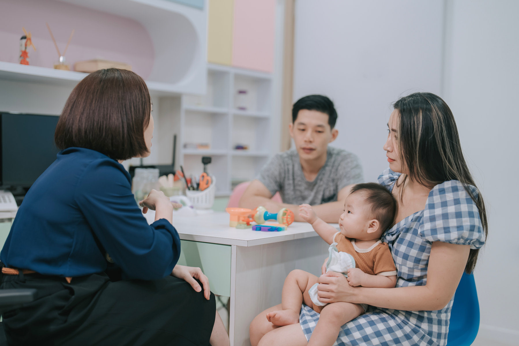 Asian Chinese female Paediatrician explaining to worried parents of baby boy in clinic