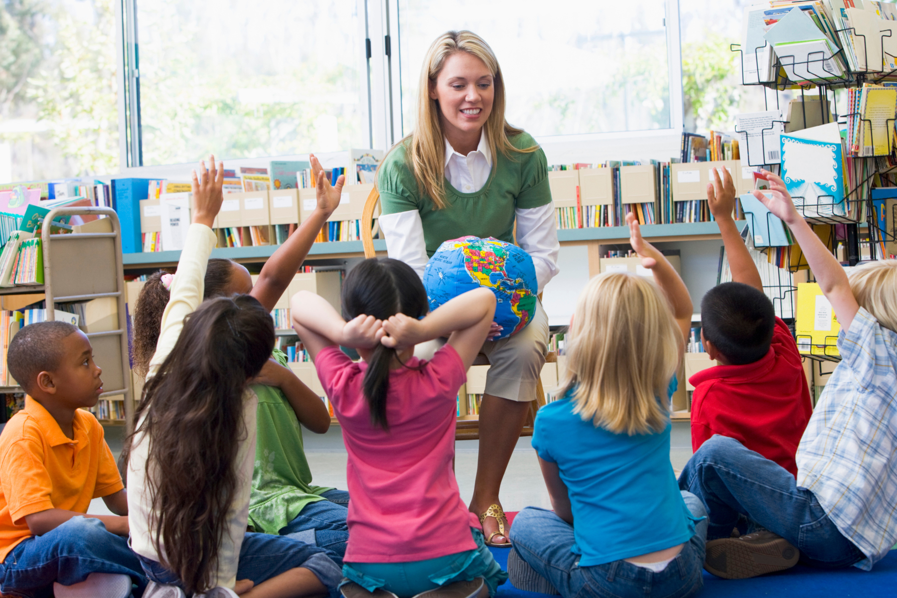 Kindergarten teacher and children with hands raised in library